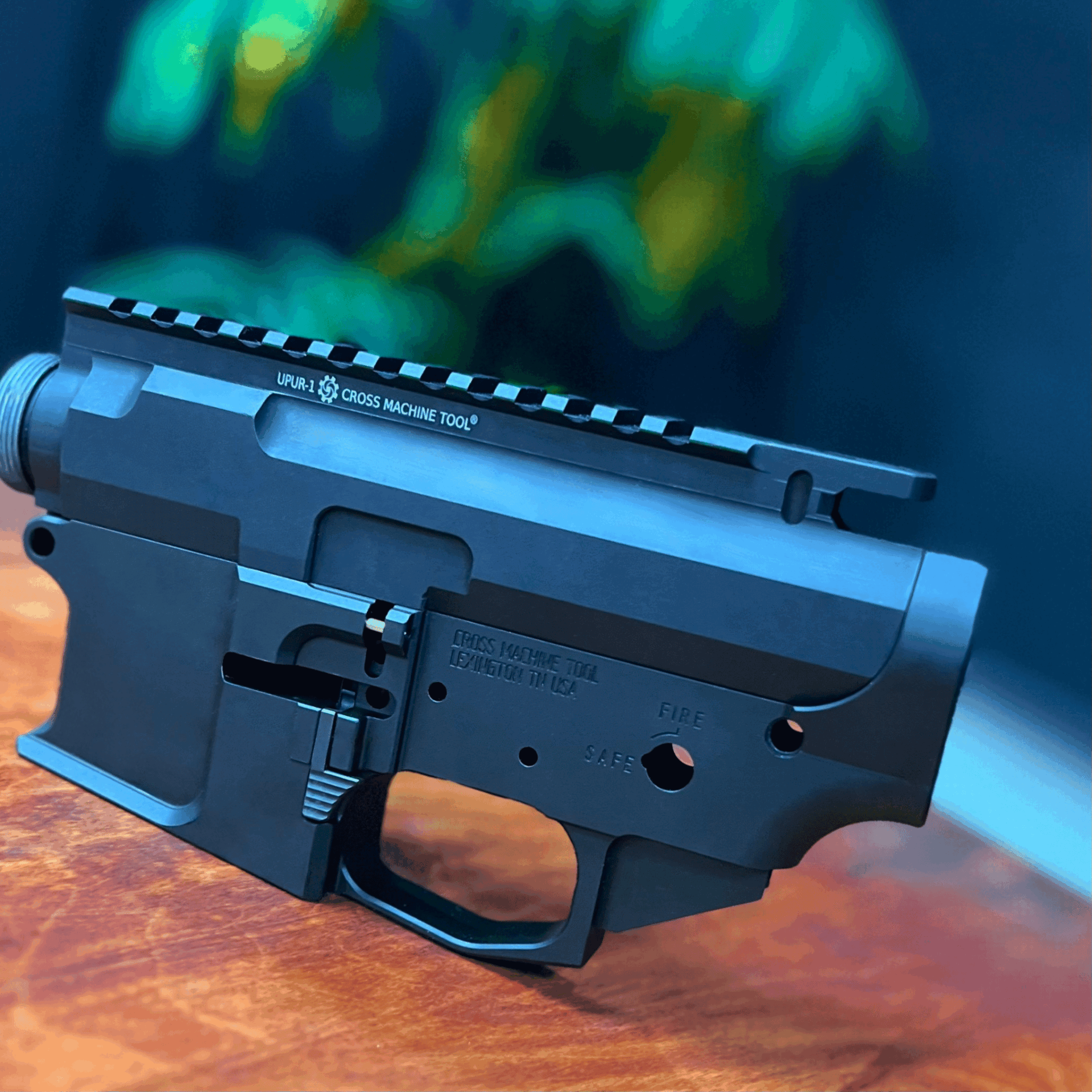 Close-up of a black firearm receiver resting on a wooden surface with a blurred green and black background.